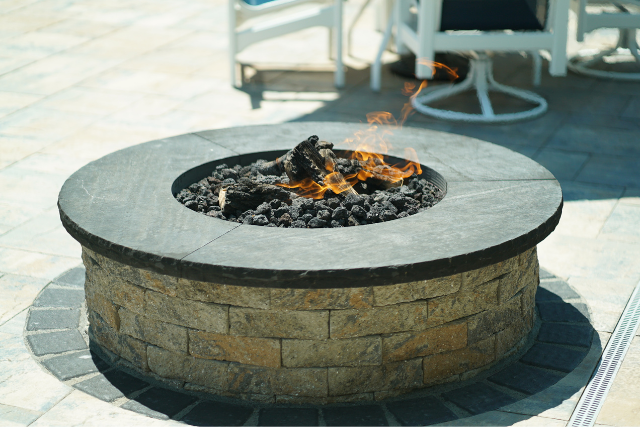 Round black sandstone fire pit with flames and stone paver base on a patio