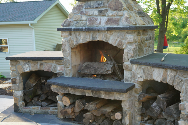 Black sandstone outdoor fireplace with stone mantle in a residential landscape