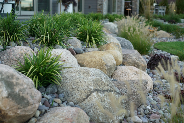 Natural stone boulder garden bed with mixed river rock, ornamental grasses, and lush plantings