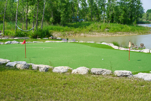 Backyard putting green bordered with limestone boulders alongside a pond with grassy banks