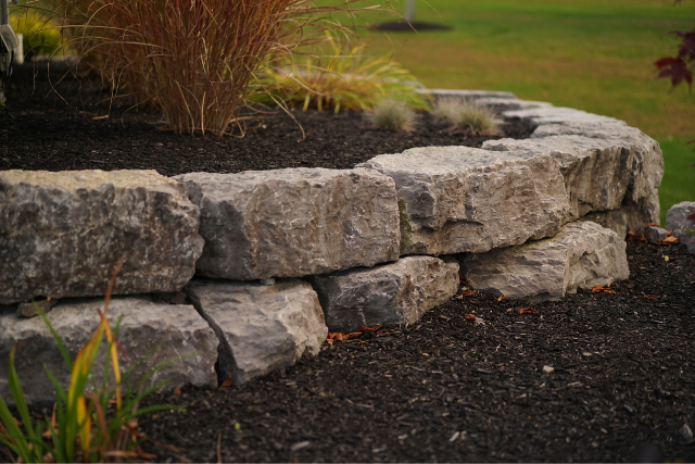Stacked limestone boulder retaining wall with ornamental grasses in a residential garden bed