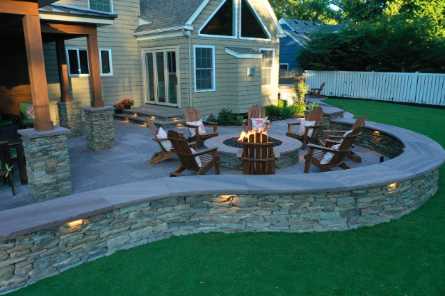 Backyard patio with brownstone seating wall, fire pit, and Adirondack chairs at dusk