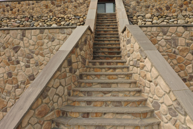 Brownstone natural stone staircase between two mosaic stone walls in a residential landscape