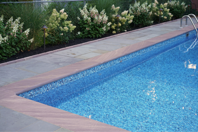 Brownstone natural stone pool coping and patio surround with poolside landscaping