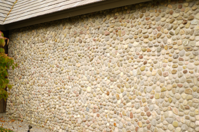 Round cobblestone wall cladding on a building exterior in mixed tan, cream, and rust colors
