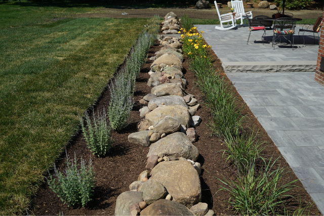 Curved cobblestone garden border separating a paver patio from lawn and landscaped plantings