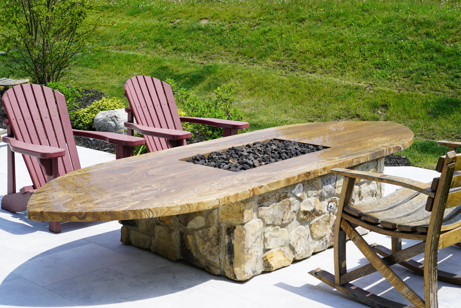 Custom fabricated oval natural stone fire pit table on a backyard patio with outdoor seating