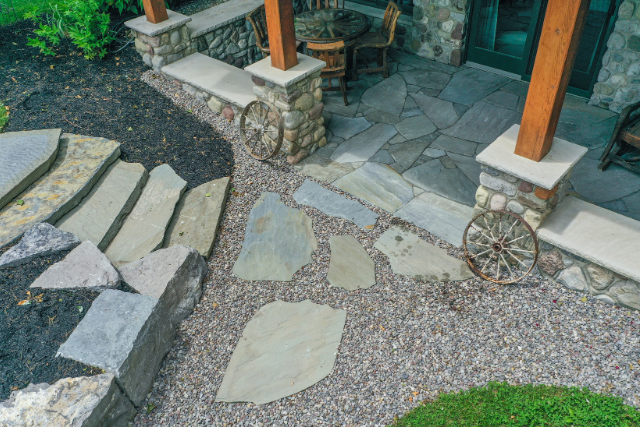 Flagstone path with wide stone slabs, gravel inlay, and stone-clad porch pillars at a rustic home