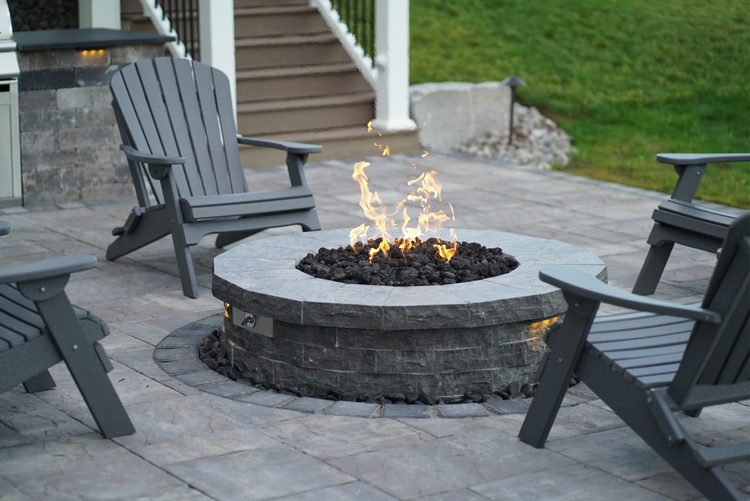 Round natural stone fire pit with flames and lava rocks on a paver patio with outdoor seating