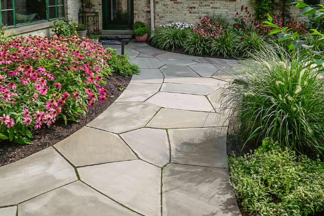 Curved bluestone flagstone walkway with garden borders of pink coneflowers and ornamental grasses