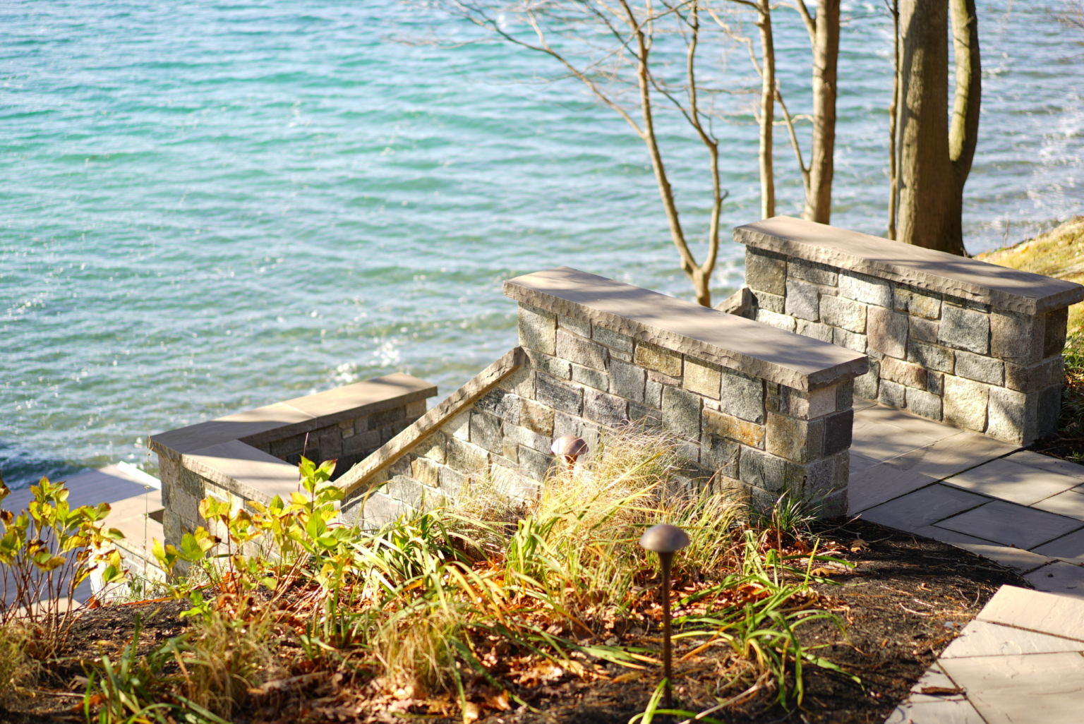 Natural stone wall with pillar caps and paver pathway at a lakeside property landscaping project