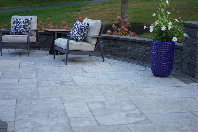 Grey pattern cut patio with stone seating wall, lounge chairs, and floral planter