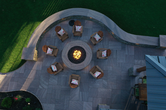 Aerial view of a curved bluestone patio with circular fire pit and Adirondack chair seating arrangement
