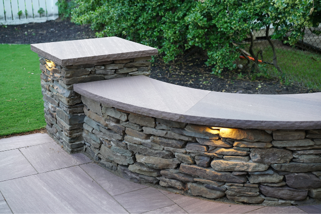 Curved natural stone seating wall with stone caps and inset lighting on a bluestone patio