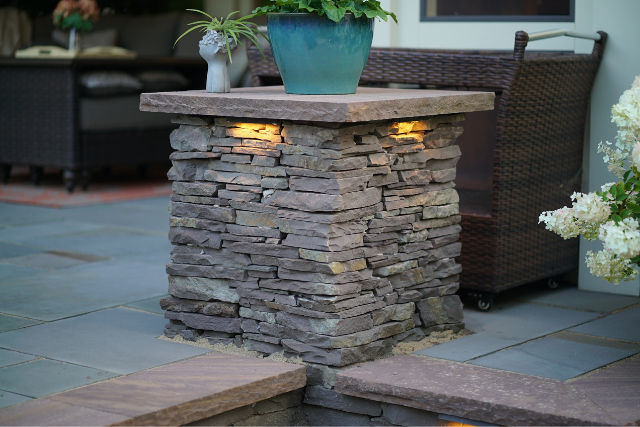 Stacked ledgestone pillar with natural stone cap and inset lighting on an outdoor patio