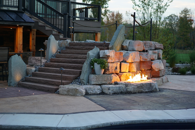 Natural stone steps with boulder fire feature and outdoor patio at dusk