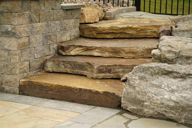 Natural stone slab steps with stacked stone wall and large boulder accent in a garden