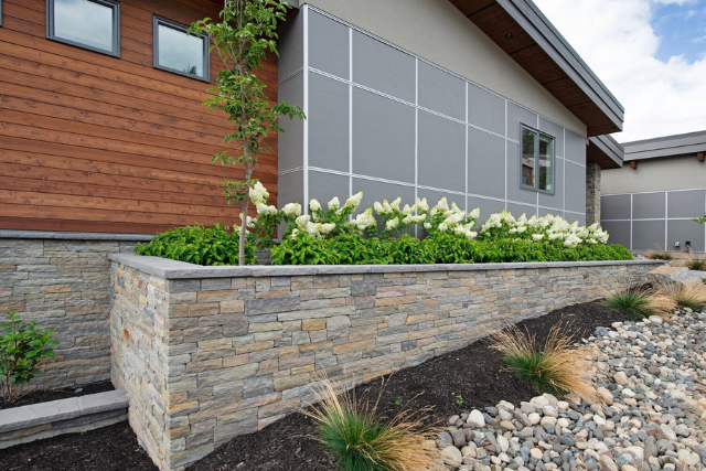 Natural stone veneer planter wall at a modern home exterior with landscaping