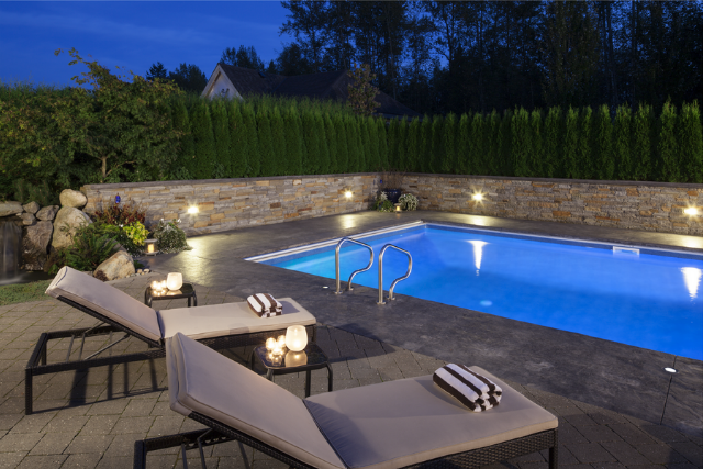 Natural stone veneer pool wall at an evening backyard pool with lounge seating