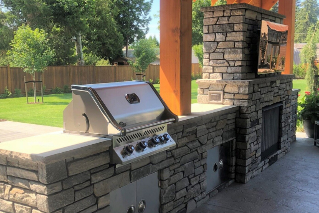 Natural stone veneer outdoor kitchen with built-in grill and stone fireplace