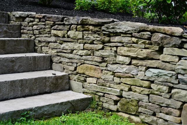 Natural stone wallstone retaining wall with steps leading into a garden landscape