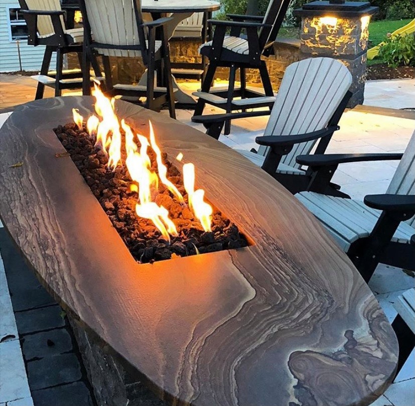 Custom fabricated natural stone fire pit with oval design and flames on an outdoor patio